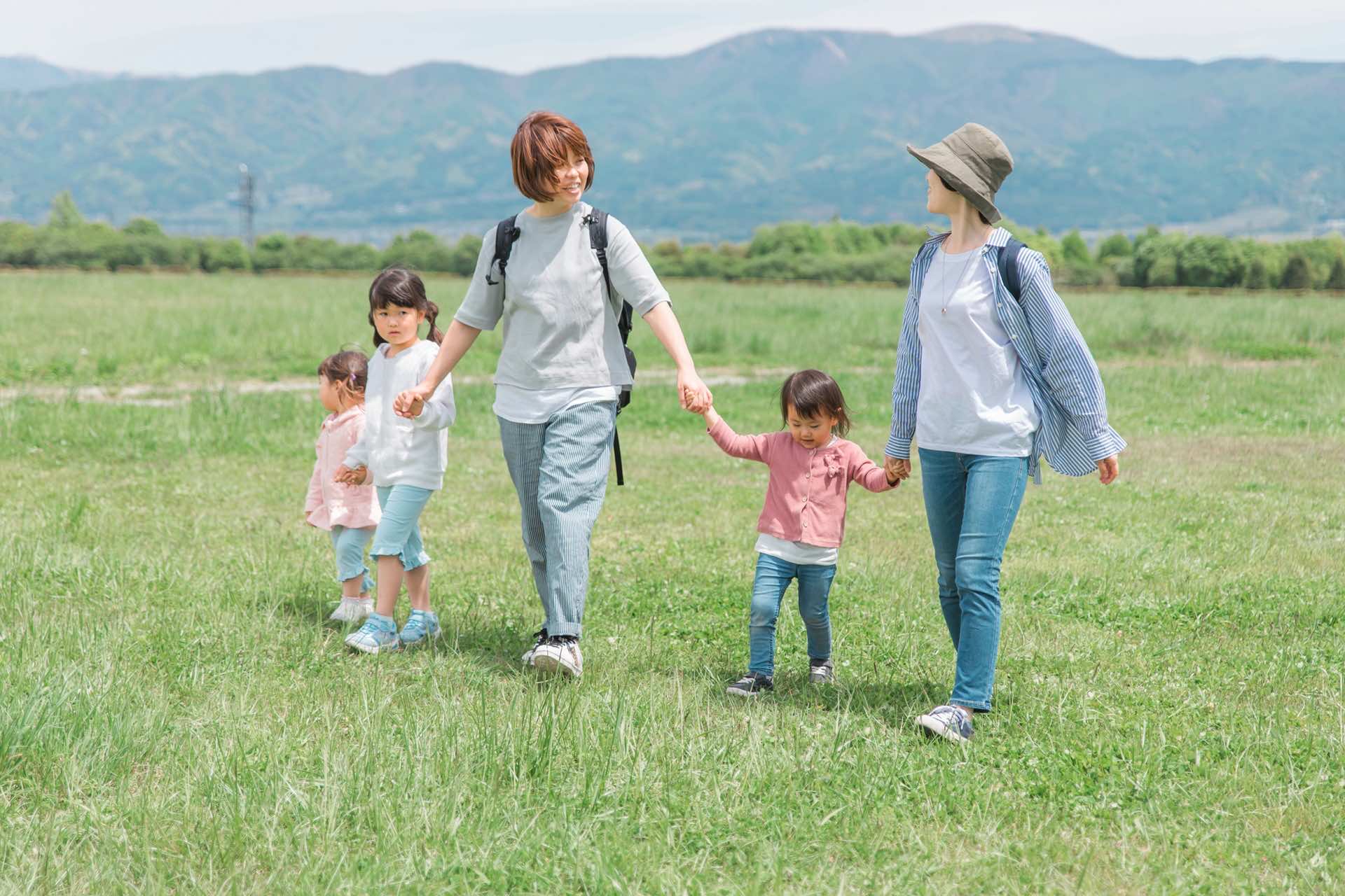 大人2人と手を繋いで草原を歩く歩く3人の子どもたち